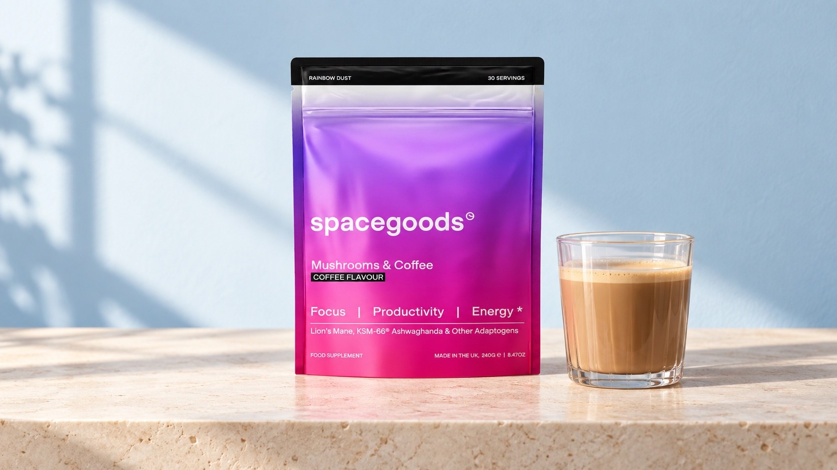 Illustration of a pink Spacegoods Rainbow Dust Coffee pouch beside a glass mug on a stone ledge against a blue wall.