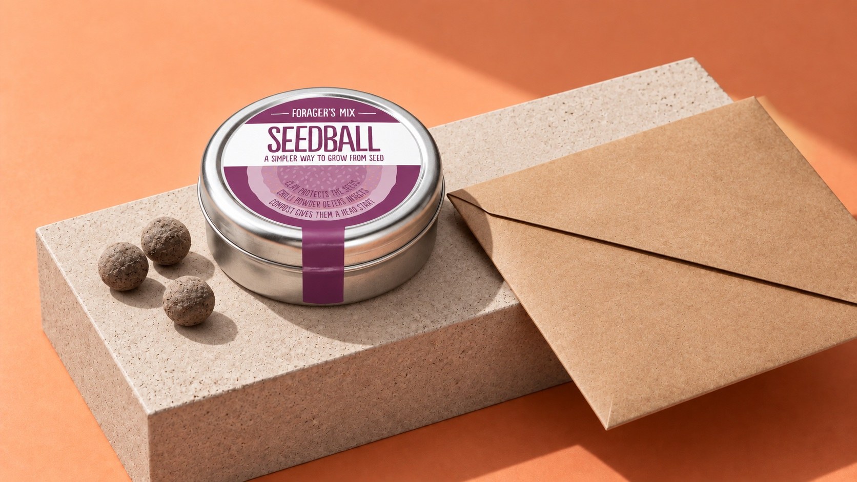 Seedball Foragers Mix tin with seed balls and a flat kraft mailing envelope on a coral background