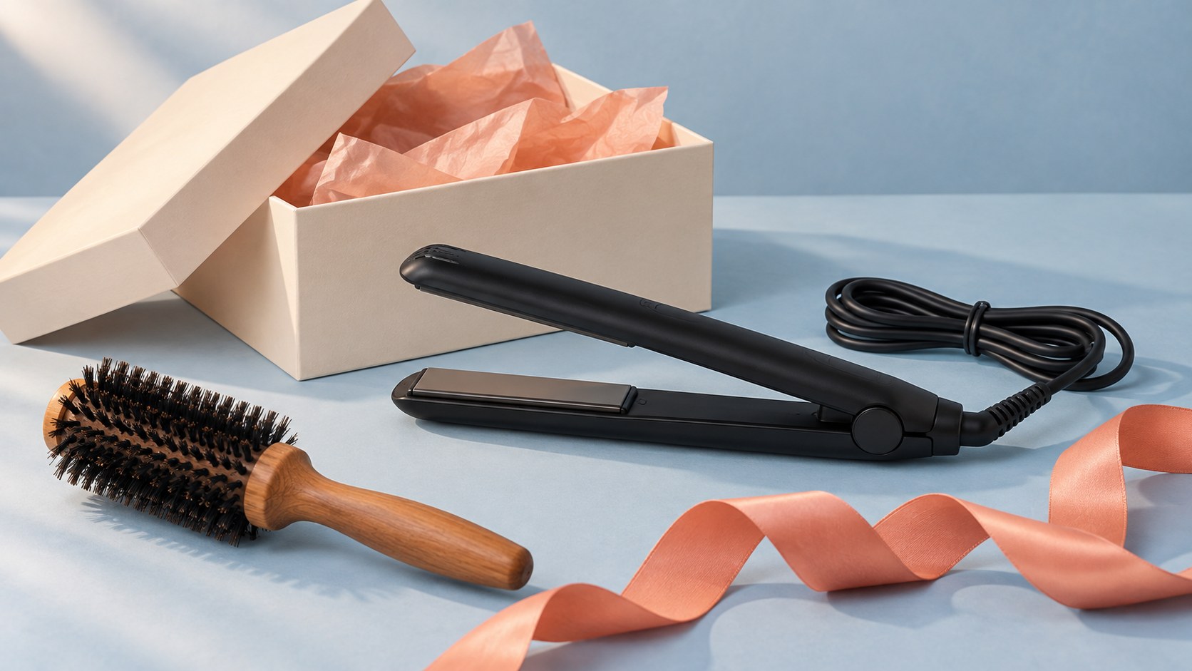 Illustration of a generic black hair straightener and round brush beside an open gift box and coral ribbon